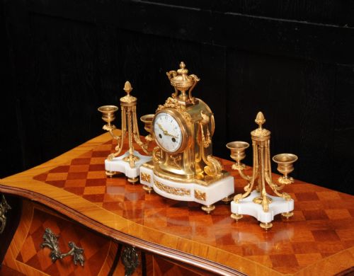 fig 5. A French Louis XVI style clock garniture set featuring a central gilt bronze and white marble mantel clock flanked by two matching two-light candelabra.