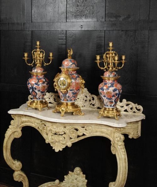fig 1. A three-piece antique French mantel garniture featuring a central Imari porcelain clock flanked by two matching gilt bronze candelabra atop porcelain urns.