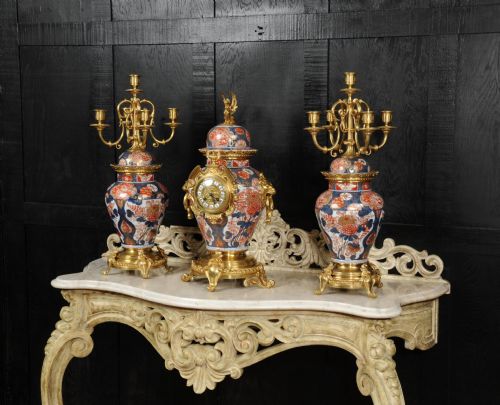 fig 2. A three-piece antique French mantel garniture featuring a central Imari porcelain clock flanked by two matching gilt bronze candelabra atop porcelain urns.