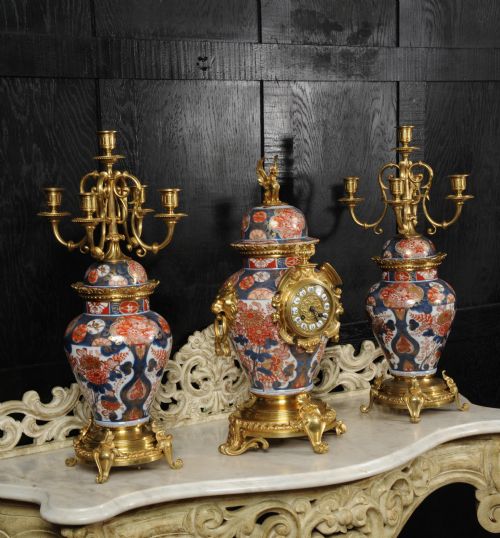 fig 3. A three-piece antique French mantel garniture featuring a central Imari porcelain clock flanked by two matching gilt bronze candelabra atop porcelain urns.