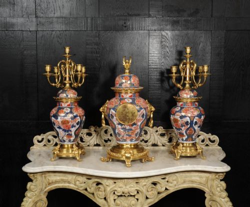 fig 4. A three-piece antique French mantel garniture featuring a central Imari porcelain clock flanked by two matching gilt bronze candelabra atop porcelain urns.