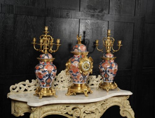 fig 5. A three-piece antique French mantel garniture featuring a central Imari porcelain clock flanked by two matching gilt bronze candelabra atop porcelain urns.