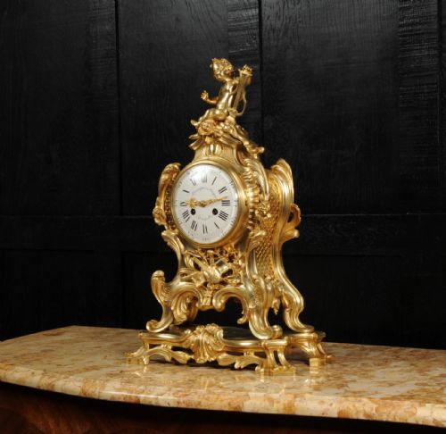 fig 2. A French Rococo gilded bronze mantel clock featuring a cherub surmount, musical instrument reliefs, and a white enamel dial.