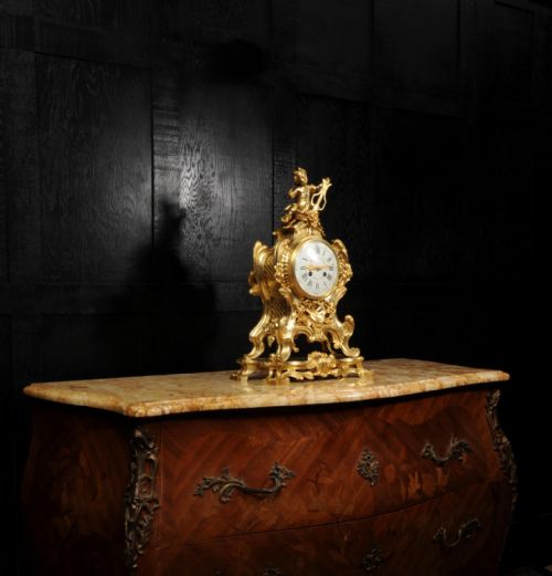 fig 4. A French Rococo gilded bronze mantel clock featuring a cherub surmount, musical instrument reliefs, and a white enamel dial.