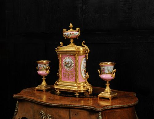 fig 2. A French nineteenth-century clock garniture set comprising a gilt bronze and pink painted porcelain mantel clock accompanied by two matching ornamental urns.
