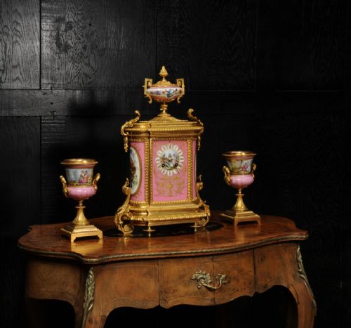 fig 3. A French nineteenth-century clock garniture set comprising a gilt bronze and pink painted porcelain mantel clock accompanied by two matching ornamental urns.