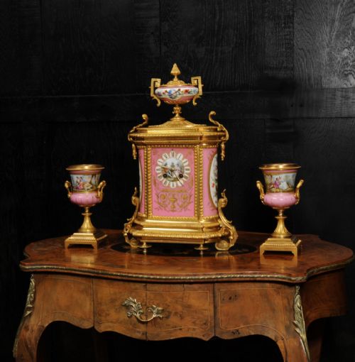 fig 4. A French nineteenth-century clock garniture set comprising a gilt bronze and pink painted porcelain mantel clock accompanied by two matching ornamental urns.