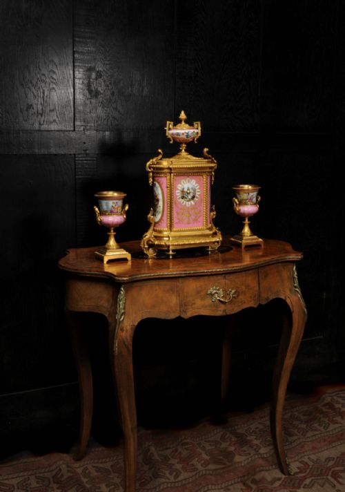fig 5. A French nineteenth-century clock garniture set comprising a gilt bronze and pink painted porcelain mantel clock accompanied by two matching ornamental urns.