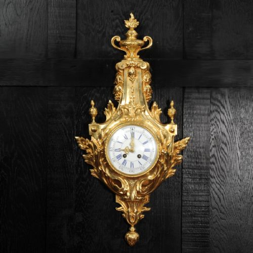 fig 1. A Louis XVI style gilt bronze cartel wall clock featuring an urn finial, detailed acanthus leaf scrolls, and a white enamel dial with Roman numerals.