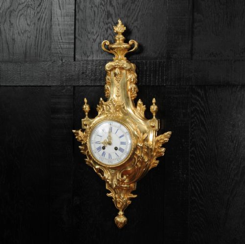 fig 2. A Louis XVI style gilt bronze cartel wall clock featuring an urn finial, detailed acanthus leaf scrolls, and a white enamel dial with Roman numerals.