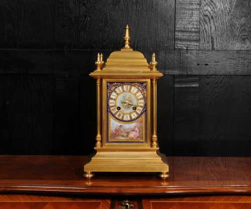 fig 1. An antique gilt bronze mantel clock featuring hand-painted floral and figure porcelain panels, corner columns, and decorative top finials.