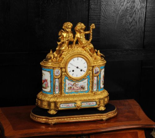 fig 3. A French gilt bronze and celeste blue porcelain mantel clock topped with two gilded cherub figures and hand-painted floral panels surrounding a white enamel dial.