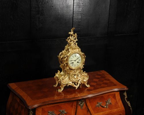 fig 2. An ornate gold gilt bronze mantel clock in the Rococo style featuring asymmetric scrollwork, acanthus leaf motifs, and a white enamel dial with black Roman numerals.