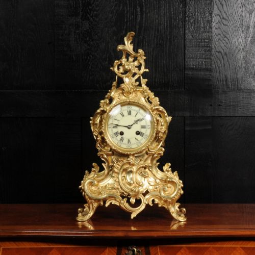 fig 3. An ornate gold gilt bronze mantel clock in the Rococo style featuring asymmetric scrollwork, acanthus leaf motifs, and a white enamel dial with black Roman numerals.