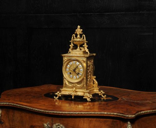 fig 2. A Louis XVI style gilt bronze mantel clock surmounted by a classical urn finial and detailed with drapery swags around a round dial.