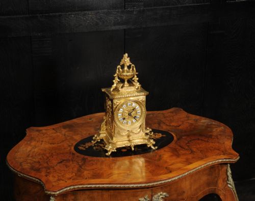 fig 3. A Louis XVI style gilt bronze mantel clock surmounted by a classical urn finial and detailed with drapery swags around a round dial.