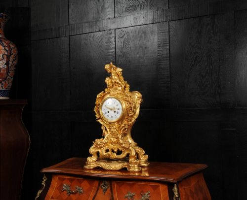 fig 1. An ornate French Rococo ormolu mantel clock decorated with an elaborate cherub finial, acanthus leaf scrolls, and a white enamel dial.