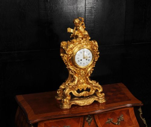 fig 2. An ornate French Rococo ormolu mantel clock decorated with an elaborate cherub finial, acanthus leaf scrolls, and a white enamel dial.