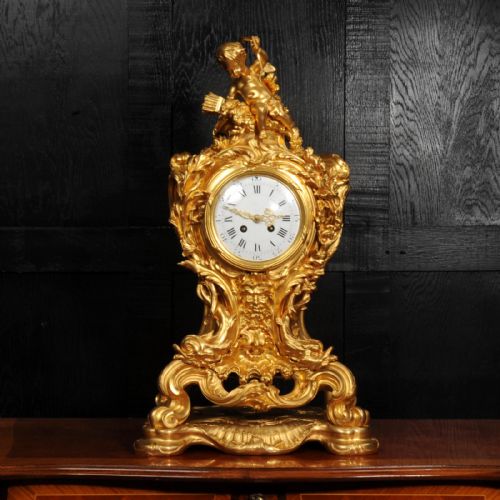 fig 5. An ornate French Rococo ormolu mantel clock decorated with an elaborate cherub finial, acanthus leaf scrolls, and a white enamel dial.