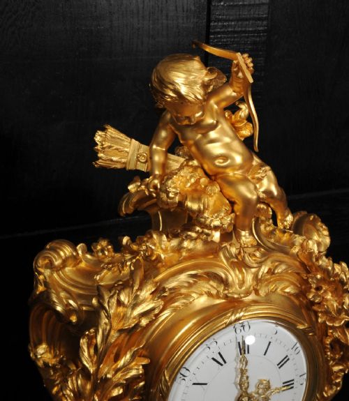 fig 8. An ornate French Rococo ormolu mantel clock decorated with an elaborate cherub finial, acanthus leaf scrolls, and a white enamel dial.