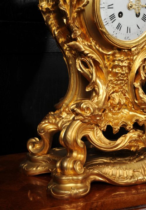 fig 9. An ornate French Rococo ormolu mantel clock decorated with an elaborate cherub finial, acanthus leaf scrolls, and a white enamel dial.