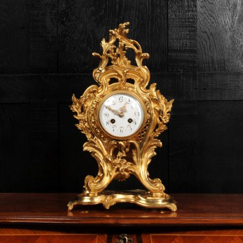 fig 1. An ornate French Rococo gilt ormolu mantel clock featuring asymmetric scrollwork, acanthus leaf details, and a white enamel dial.