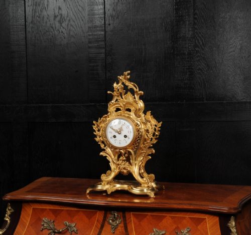 fig 2. An ornate French Rococo gilt ormolu mantel clock featuring asymmetric scrollwork, acanthus leaf details, and a white enamel dial.