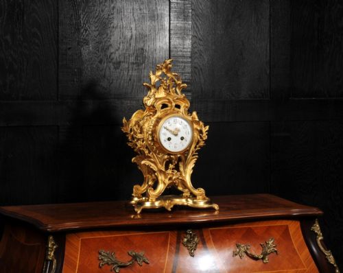 fig 3. An ornate French Rococo gilt ormolu mantel clock featuring asymmetric scrollwork, acanthus leaf details, and a white enamel dial.