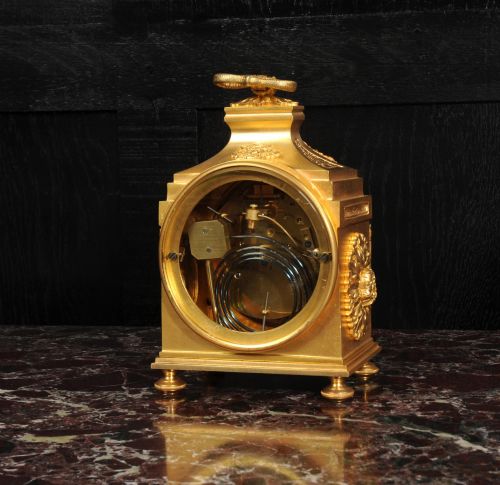 fig 8. An antique French gilt bronze ormolu officer clock with a ribbon top handle, decorative floral swags, and a white enamel dial with Arabic numerals.