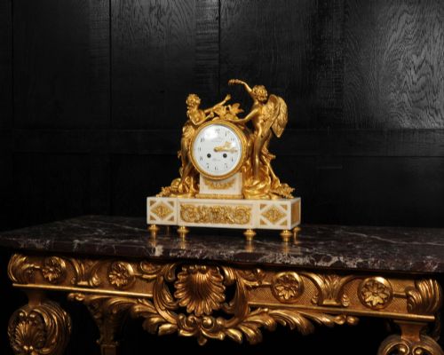 fig 1. An antique French ormolu and white marble mantel clock featuring gilt bronze figures of Cupid and Psyche surrounding a central white enamel dial on a rectangular marble base.