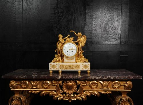 fig 2. An antique French ormolu and white marble mantel clock featuring gilt bronze figures of Cupid and Psyche surrounding a central white enamel dial on a rectangular marble base.