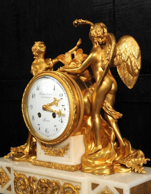 fig 3. An antique French ormolu and white marble mantel clock featuring gilt bronze figures of Cupid and Psyche surrounding a central white enamel dial on a rectangular marble base.