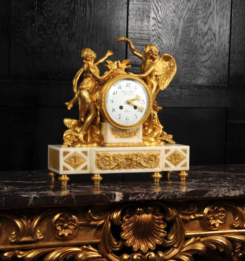fig 5. An antique French ormolu and white marble mantel clock featuring gilt bronze figures of Cupid and Psyche surrounding a central white enamel dial on a rectangular marble base.