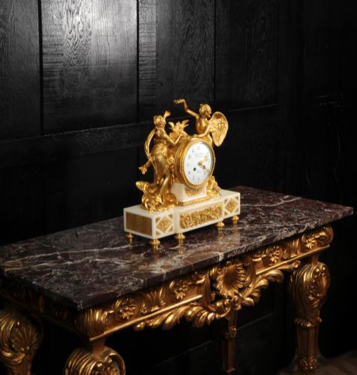 fig 6. An antique French ormolu and white marble mantel clock featuring gilt bronze figures of Cupid and Psyche surrounding a central white enamel dial on a rectangular marble base.