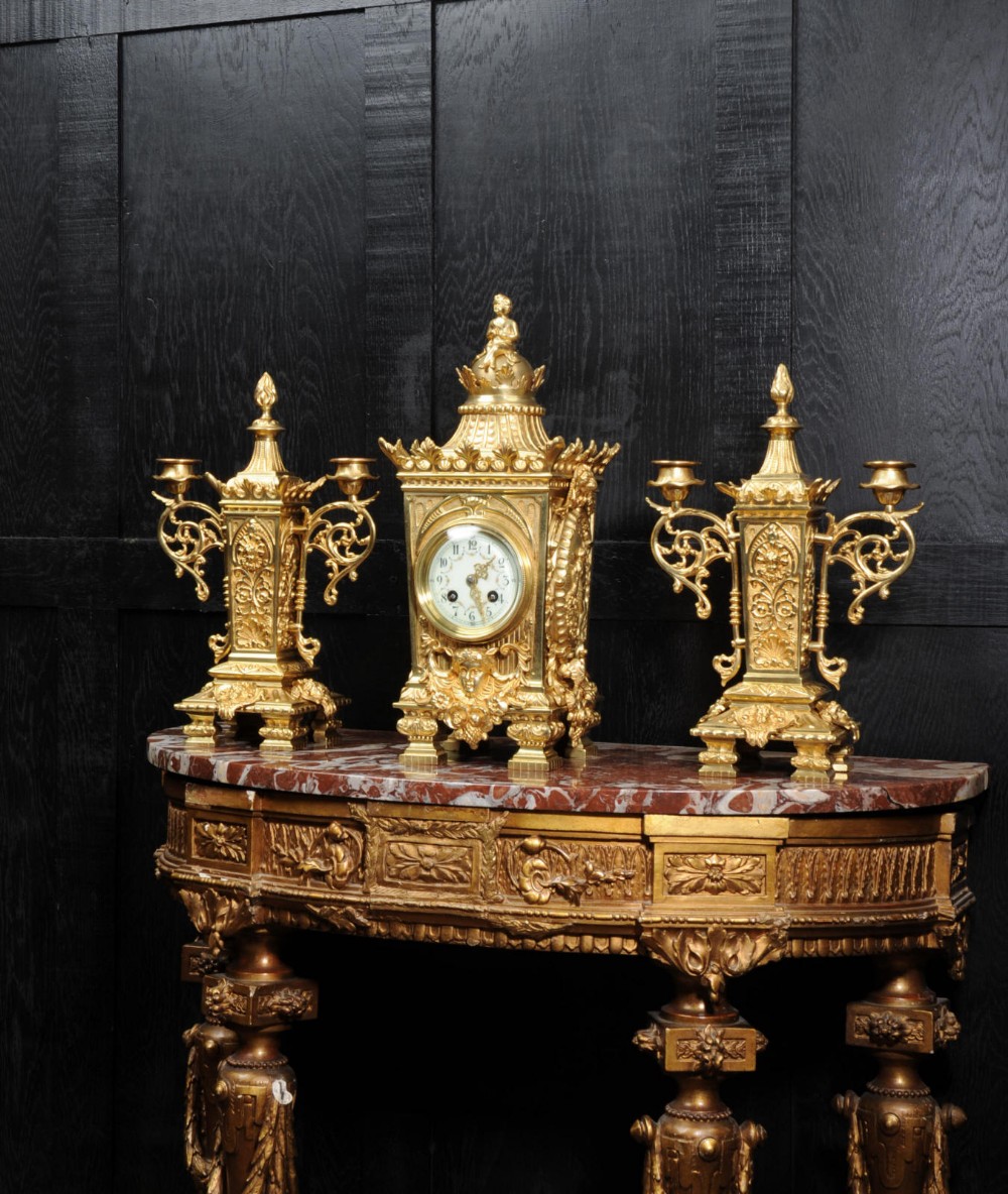 A three-piece Louis XVI style gilt bronze clock garniture set comprising a central urn-topped mantel clock flanked by two matching side candelabra.