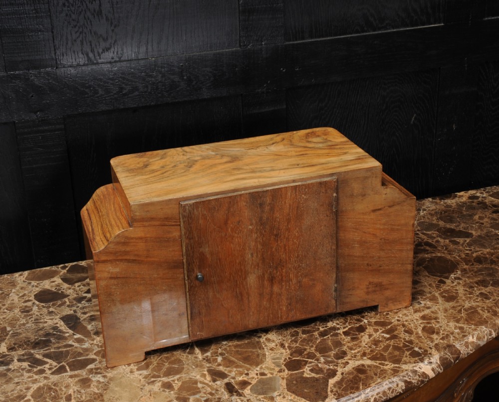 An Art Deco mantel clock featuring a figurative walnut veneered wooden case with stepped sides and a rectangular silver-toned dial with bold black numerals. View VIII