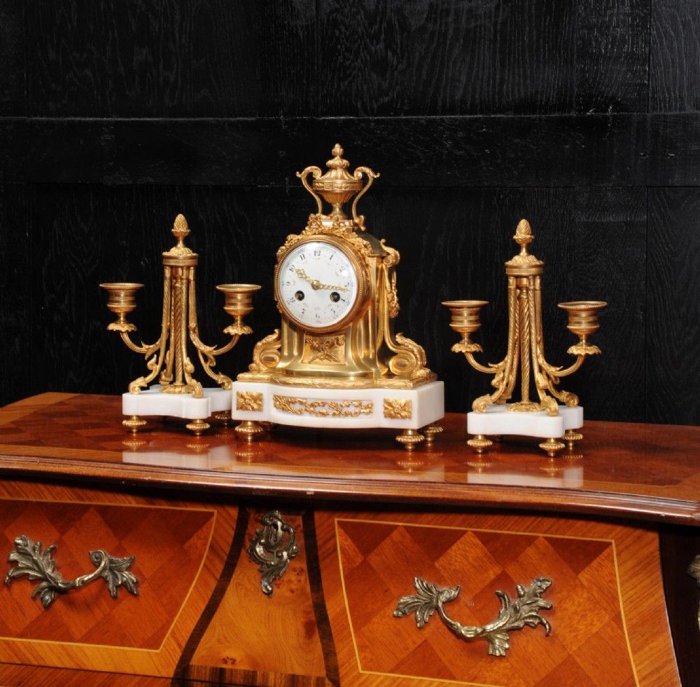A French Louis XVI style clock garniture set featuring a central gilt bronze and white marble mantel clock flanked by two matching two-light candelabra.