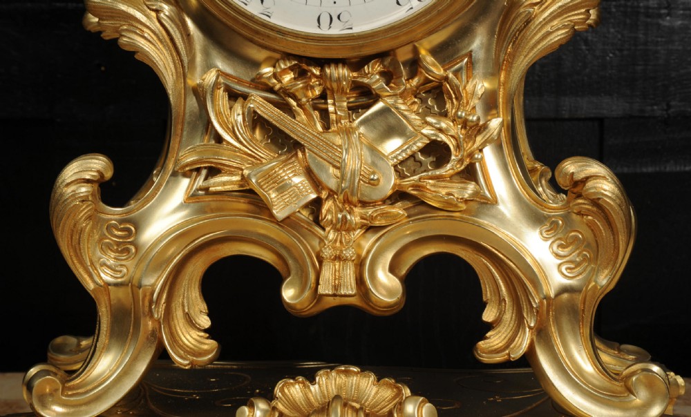 A French Rococo gilded bronze mantel clock featuring a cherub surmount, musical instrument reliefs, and a white enamel dial. View XVIII