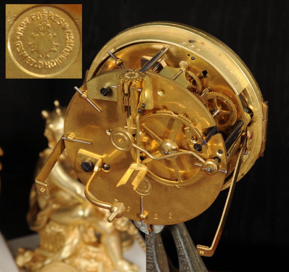 An antique French mantel clock featuring a white marble base decorated with gilt bronze mounts, an off-centre enamel dial, and a gilded bronze putto figure seated alongside. View XV