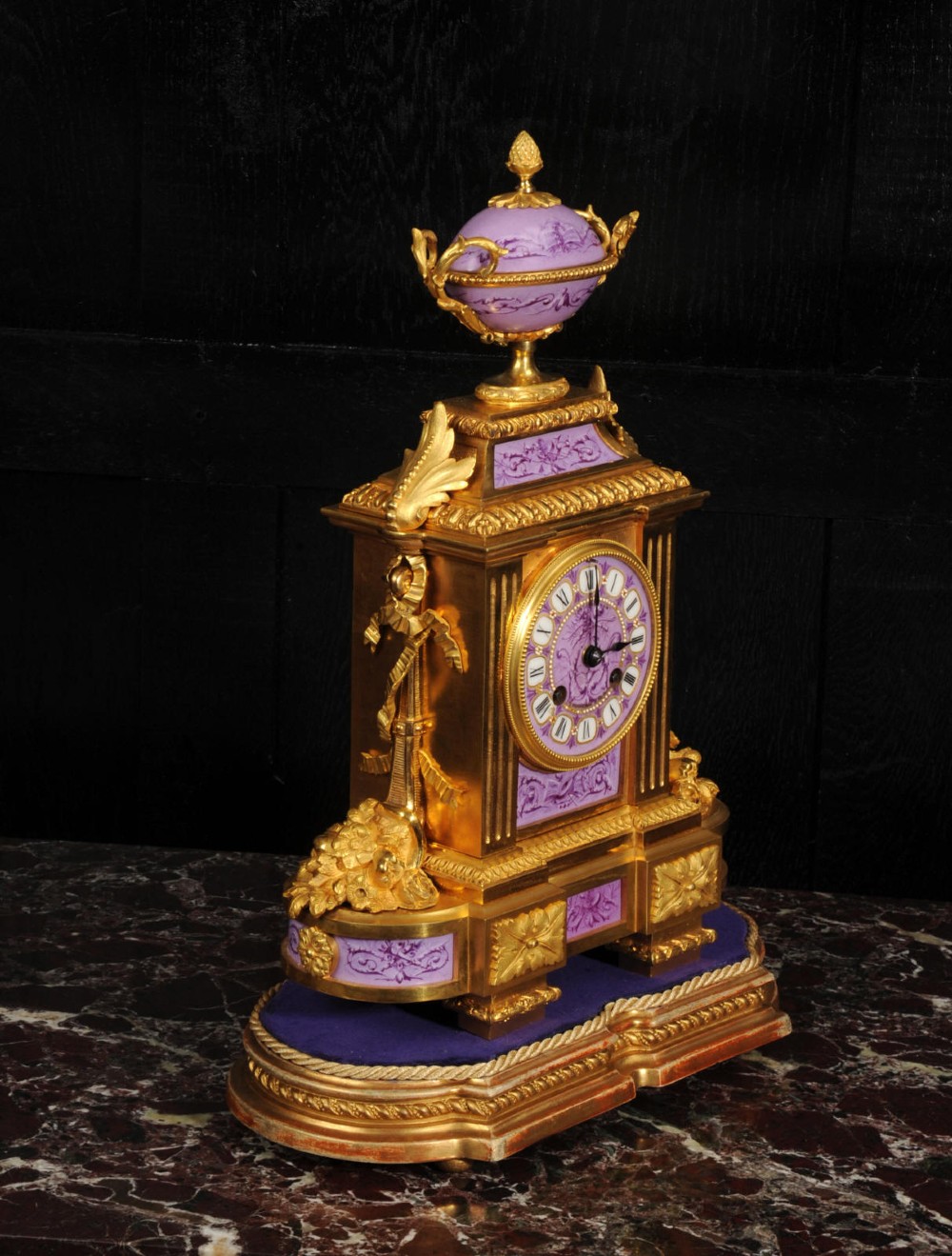 An ornate French gilt bronze and lilac hand-painted porcelain mantel clock featuring a decorative urn finial and fluted side columns. View VI