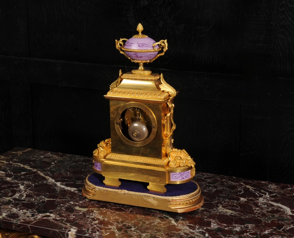 An ornate French gilt bronze and lilac hand-painted porcelain mantel clock featuring a decorative urn finial and fluted side columns. View XV