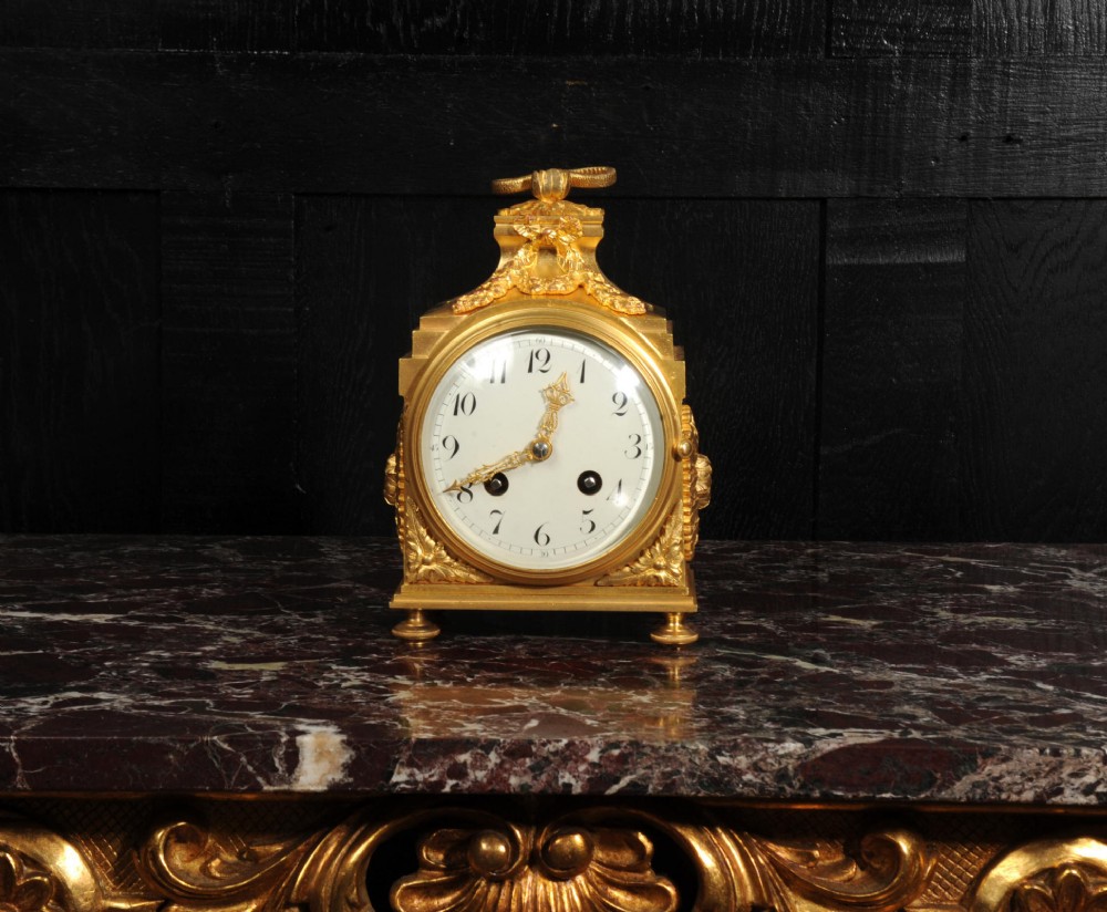 An antique French gilt bronze ormolu officer clock with a ribbon top handle, decorative floral swags, and a white enamel dial with Arabic numerals. View II