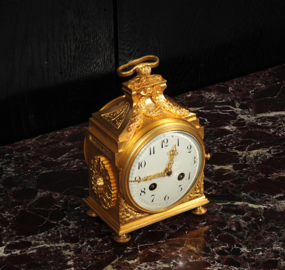 An antique French gilt bronze ormolu officer clock with a ribbon top handle, decorative floral swags, and a white enamel dial with Arabic numerals. View III