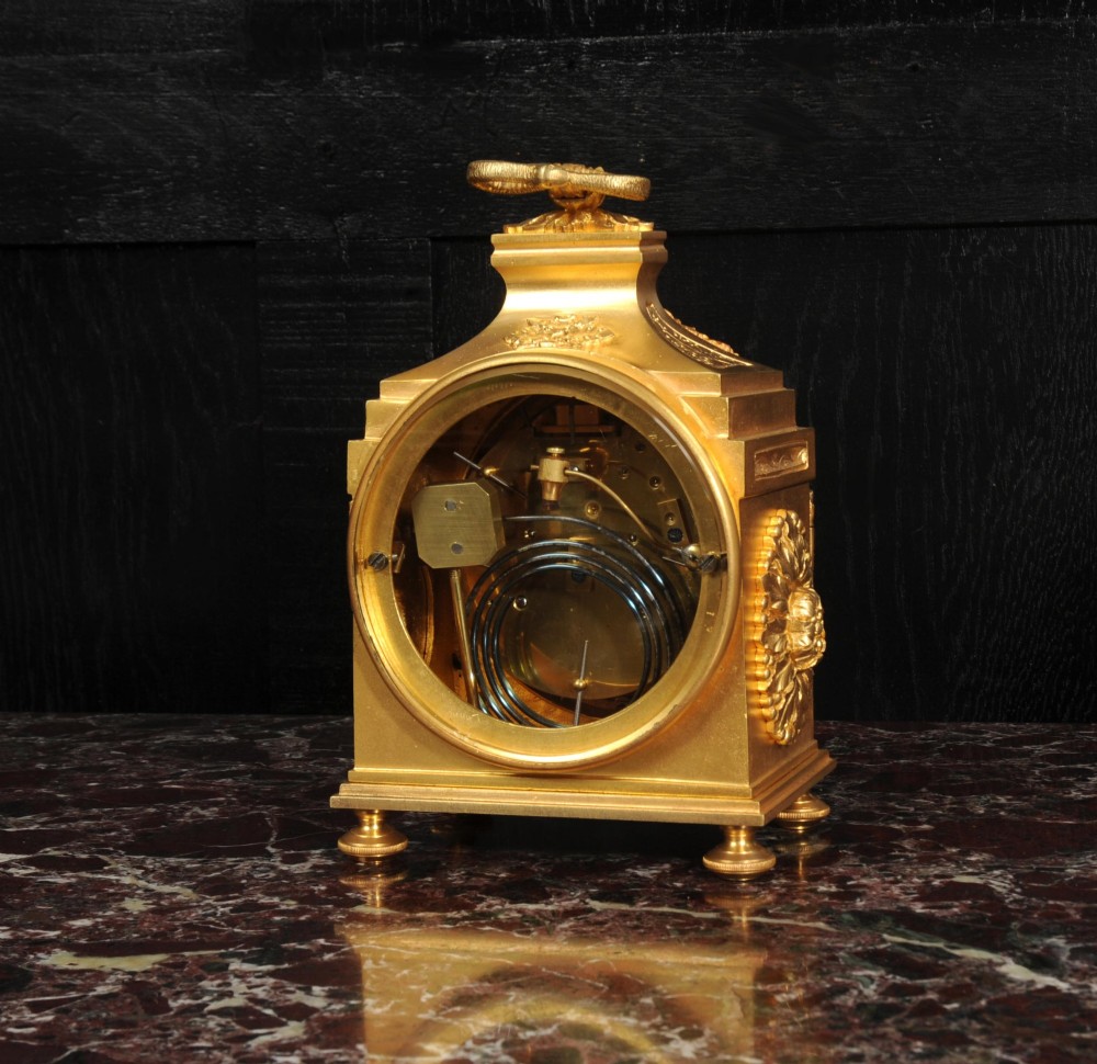 An antique French gilt bronze ormolu officer clock with a ribbon top handle, decorative floral swags, and a white enamel dial with Arabic numerals. View IX