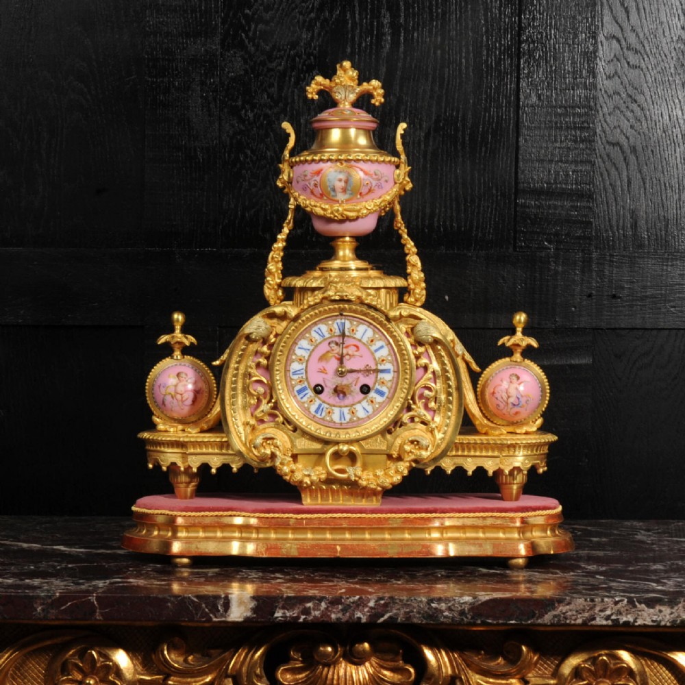 An ornate 19th-century French gilt-bronze and pink Sevres porcelain mantel clock featuring scrolled ormolu mounts and hand-painted cherubs.