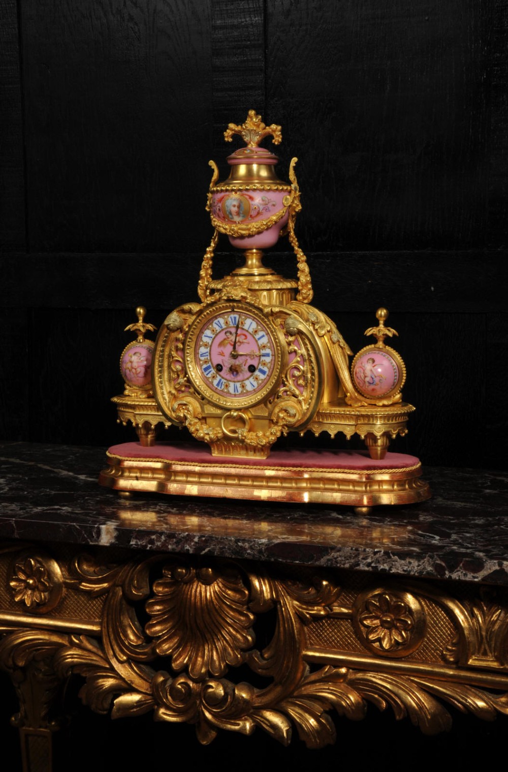 An ornate 19th-century French gilt-bronze and pink Sevres porcelain mantel clock featuring scrolled ormolu mounts and hand-painted cherubs. View V