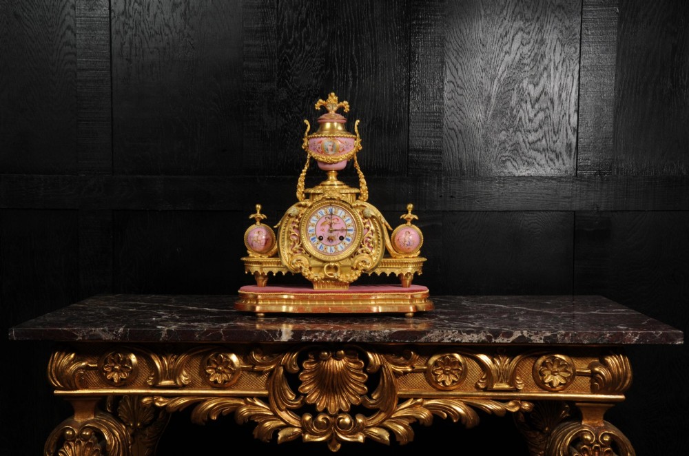 An ornate 19th-century French gilt-bronze and pink Sevres porcelain mantel clock featuring scrolled ormolu mounts and hand-painted cherubs. View VI