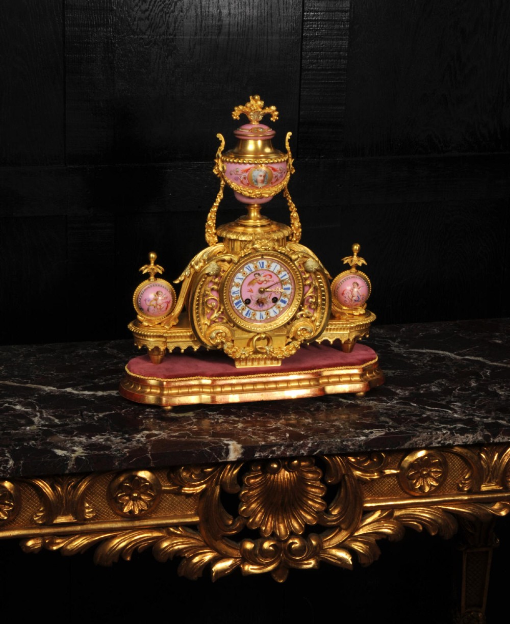 An ornate 19th-century French gilt-bronze and pink Sevres porcelain mantel clock featuring scrolled ormolu mounts and hand-painted cherubs. View VII
