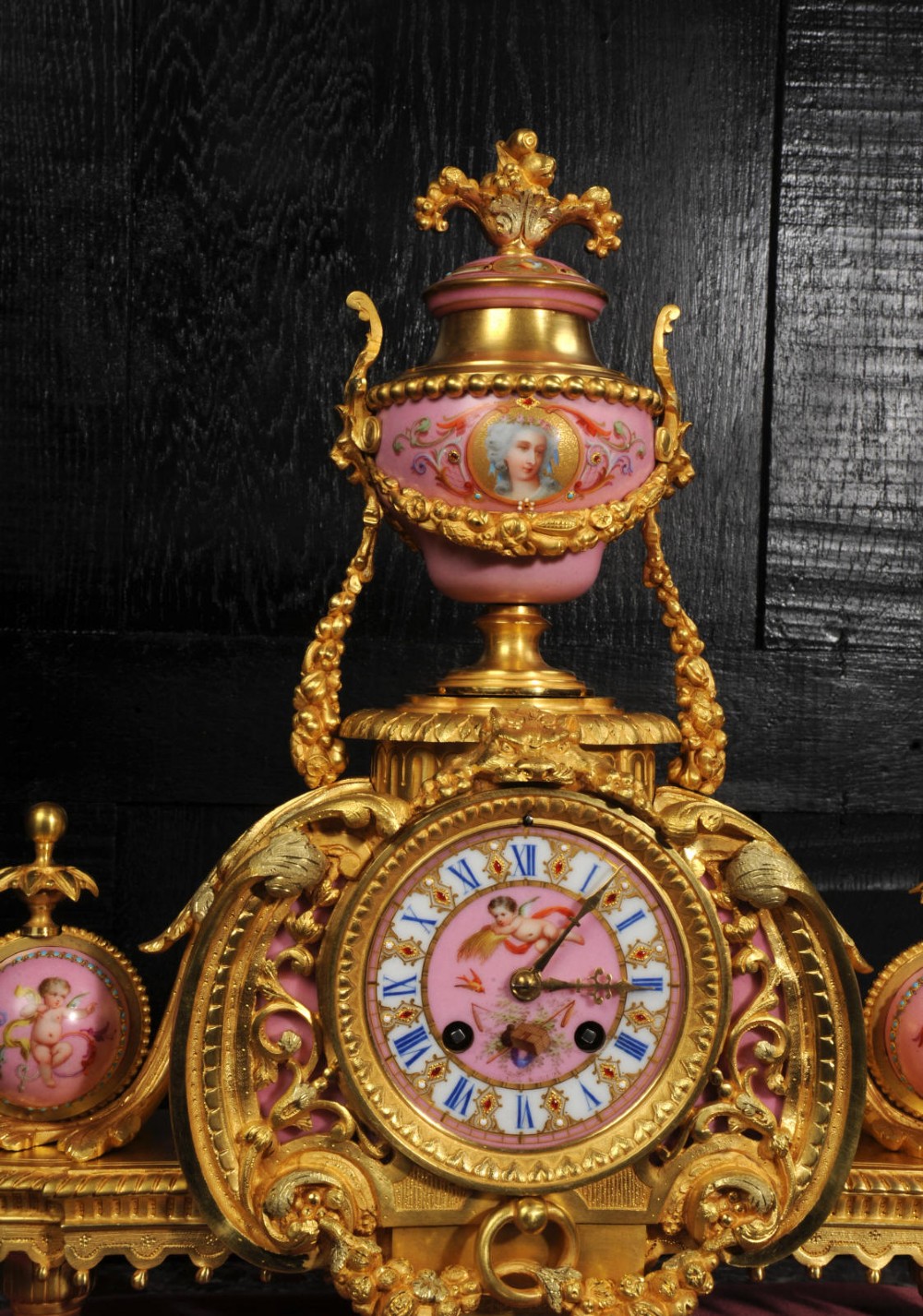 An ornate 19th-century French gilt-bronze and pink Sevres porcelain mantel clock featuring scrolled ormolu mounts and hand-painted cherubs. View X
