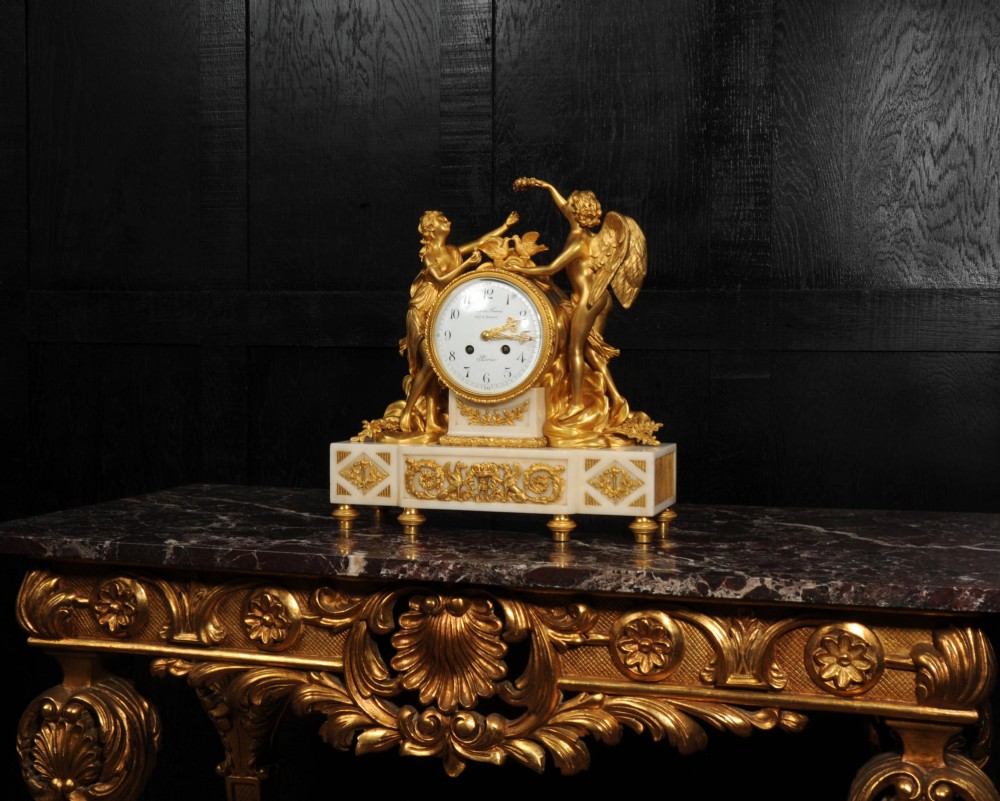 An antique French ormolu and white marble mantel clock featuring gilt bronze figures of Cupid and Psyche surrounding a central white enamel dial on a rectangular marble base. View II